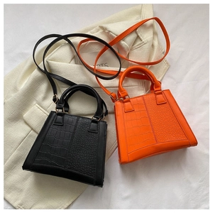 Detail of elegant crocodile pattern trapezoid handbags in black and bright orange leather