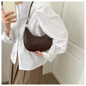 Detail shot of a dark brown crocodile embossed leather shoulder bag on a model
