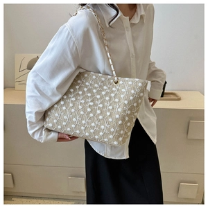 Dettaglio della borsa tote tessuta a mano con ricami floreali bianchi e tracolla a catena oro