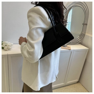 Fashionable black leather underarm bag worn by a model in a minimalist indoor setting