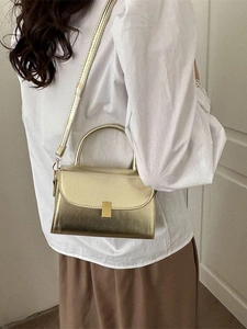 Glossy gold crossbody handbag with metallic finish and top handle on a female model