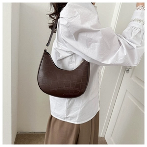 Detail of dark brown croc-effect hobo bag worn on shoulder by a model indoors