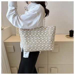 Dettaglio della borsa tote in paglia con ricamo in pizzo floreale bianco e catena dorata