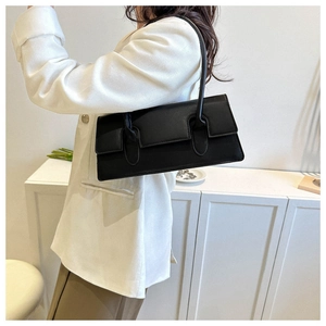 Minimalist black baguette bag with smooth matte finish worn by model in a chic room