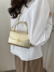 Minimalist light gold crossbody bag with glossy finish and top handle on female model