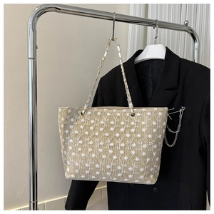 Dettaglio dei ricami floreali bianchi sulla borsa tote in paglia intrecciata beige