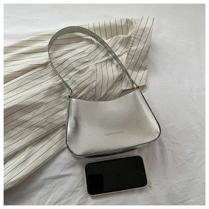 Detail of silver metallic crescent shoulder bag showing sleek texture and scale with a phone