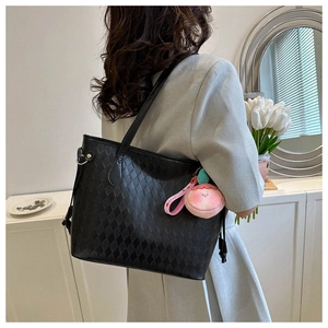 Detail of black quilted tote bag with a pink peach plush charm and long shoulder strap