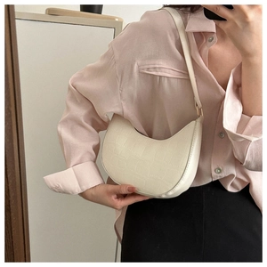 Detail of cream-colored croc-embossed crescent shoulder bag on model for casual styling