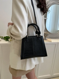 Chic black trapezoid crossbody bag with crocodile texture shown in a minimalist room