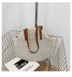 Detail of woven straw tote bag featuring wavy rim and brown faux leather handles