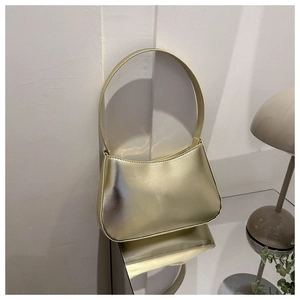 Glossy gold underarm bag with metallic finish displayed on a modern interior tabletop