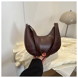 Detail shot of a dark brown crescent bag featuring crocodile embossed texture and leather strap