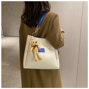 Detail of cream tote bag with blue straps, golden chain, and cute brown bear charm