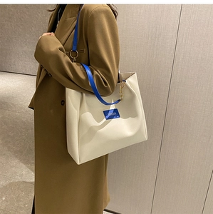 Detail of white tote bag with blue straps, golden chain, and fashion lettering tag