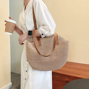 Straw woven tote bag with brown leather straps shown on model in a warm interior