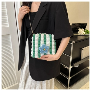 Detail view of green striped bubble tote bag with blue plush flower and gold chain