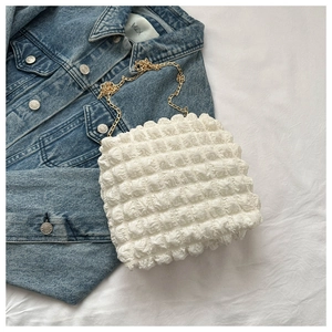 Detailed view of white popcorn texture bag with gold chain over denim jacket