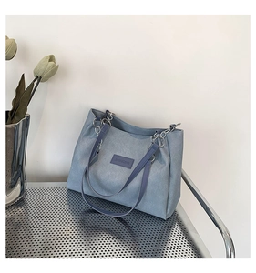 Close-up of a blue canvas tote bag featuring a leather logo patch and silver chain strap