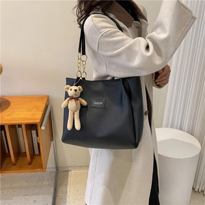 Chic black faux leather tote bag with a cute bear charm, styled for daily commute