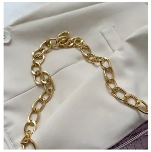 Detail of high-polish light gold alloy chain strap on a purple crocodile pattern bag