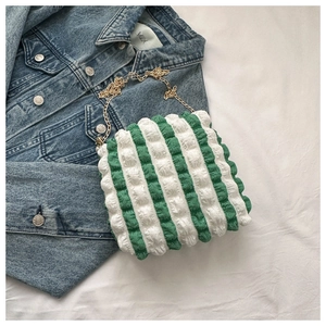 Detail of green and white striped bubble texture bag with a gold chain strap on denim