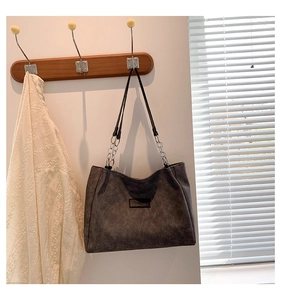 Detail of grey tote bag with vintage texture, chain strap, and logo plate on wood hook