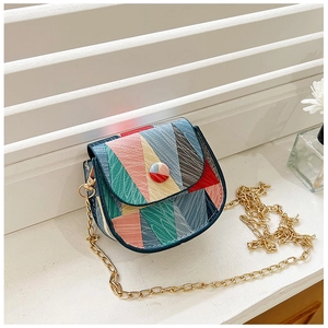 Detail of color-block flap bag with gold chain strap on a white textured surface