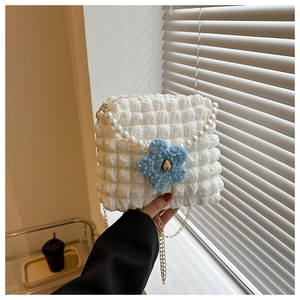 Detail of white textured puff crossbody bag with pearl strap and blue plush flower