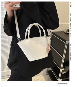 White minimalist bucket bag with woven handle and flower charm shown on model