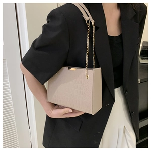 Detail of beige faux crocodile leather texture and gold chain on women shoulder bag