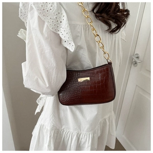 Detail of burgundy crocodile-embossed shoulder bag with a gold chain strap on a white dress