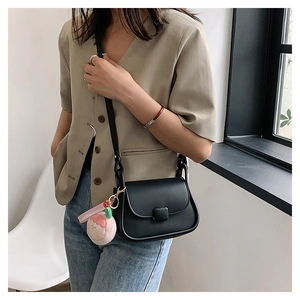 Sac bandoulière chic en cuir PU noir avec un pendentif pêche en peluche sur un mannequin