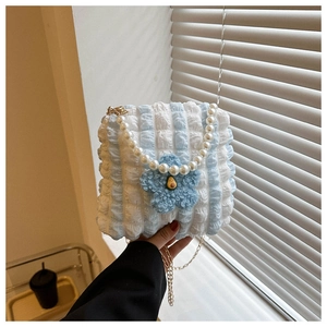 Detail of blue bubble fabric bag with pearl handle, plush flower, and avocado charm