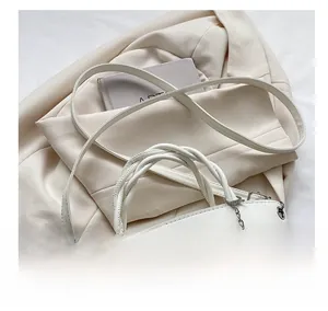 Detail of white semi-circular handbag with woven handle and pink flower charm
