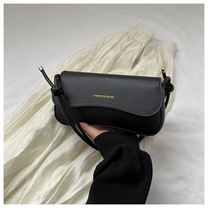 Detail of black leather shoulder bag with gold lettering and knotted strap design