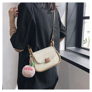 Petit sac bandoulière crème avec bords marrons et breloque pêche porté par le mannequin