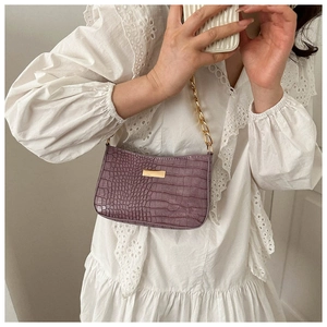 Detail of purple croc-embossed underarm bag with gold chain strap on white lace dress