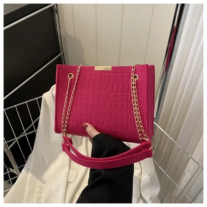 Detail of rose red crocodile embossed texture and gold chain on leather handbag