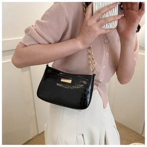 Detail of black crocodile embossed shoulder bag with gold chunky chain strap on model