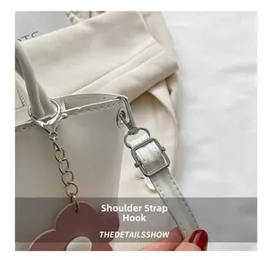 Detail of white leather bag with silver metal hooks and a pink floral charm accessory