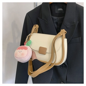 Détail du mini sac bandoulière blanc cassé avec bordure brune et breloque pêche