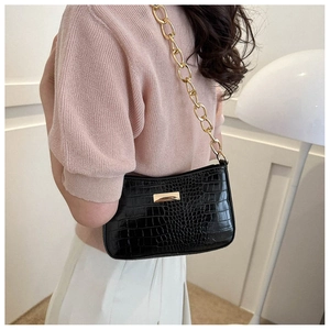Detail of black crocodile texture bag with gold chain strap worn on the shoulder