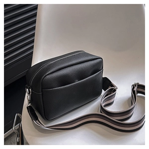 Detail view of black lychee texture PU crossbody bag with wide striped fabric strap