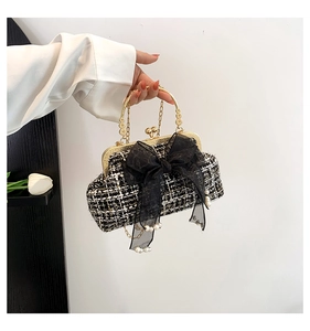 Close-up of elegant black and white tweed handbag with golden lace and pearl bow detail