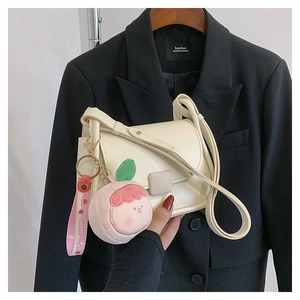 Gros plan d'un sac besace crème avec un pendentif pêche en peluche et ruban doux