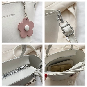 Detail of white leather bucket bag with zipper closure, floral charm and interior space