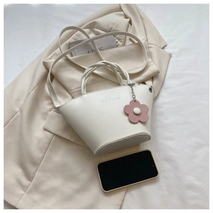 Detail of white leather bucket bag with pink flower charm and detachable strap on beige blazer