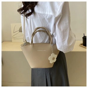 Detail of light khaki tote bag with woven handles and daisy charm worn with a long skirt