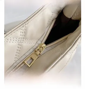 Close-up of smooth gold metal zipper and beige quilted texture on the shoulder bag